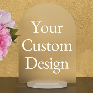 May include: A frosted acrylic sign with a rounded top and a white base. The sign is beige and has the text "Your Custom Design" in white.