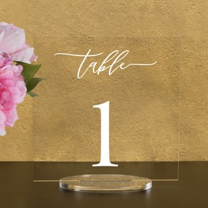 May include: Clear acrylic table number holder with the word "table" and the number "1" in white lettering.