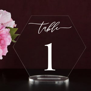 May include: A clear acrylic hexagonal table number holder with the word "Table" and the number "1" printed in white.