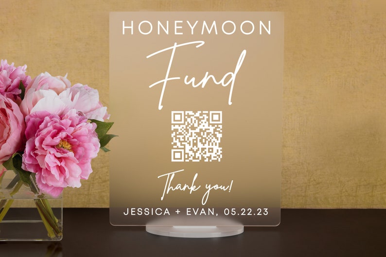 May include: A clear acrylic sign with a gold gradient background. The sign reads "Honeymoon Fund" in white cursive text. A QR code is displayed below the text, followed by "Thank you!" and "JESSICA + EVAN, 05.22.23".