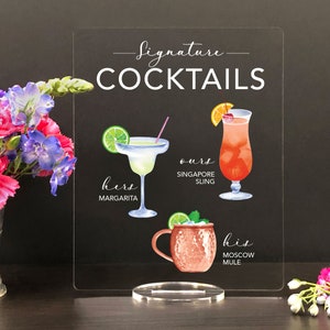May include: A clear acrylic sign with the text "Signature Cocktails" in white. The sign features three illustrated cocktails: a margarita, a Singapore Sling, and a Moscow Mule.