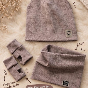 Könnte beinhalten: Ein mauvefarbenes Strickset bestehend aus einer Mütze, einem Loop-Schal und fingerlosen Handschuhen. Jedes Teil hat ein kleines rechteckiges Etikett mit dem Text FUN TIME! in Schwarz. Die Mütze ist abgerundet, der Loop ist röhrenförmig und die Handschuhe haben Daumenlöcher.