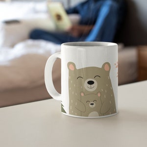 May include: White ceramic mug with a brown bear and a smaller brown bear cub hugging. The bears have smiling faces and are surrounded by green foliage.
