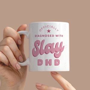 May include: White ceramic mug with a pink design that says "Officially Diagnosed With Slay DHD".