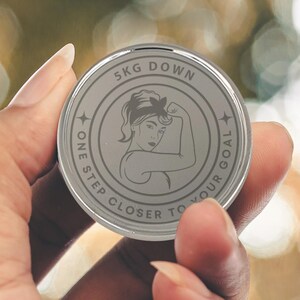 Puede incluir: Un token redondo plateado con el texto "5KG DOWN ONE STEP CLOSER TO YOUR GOAL" y una imagen estilizada de una mujer con una diadema y una expresi&oacute;n decidida.