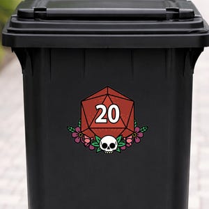 May include: A black trash can with a decorative sticker featuring a red twenty-sided die, a skull, and floral accents. The number 20 is displayed in white. The sticker is centered on the front of the can.