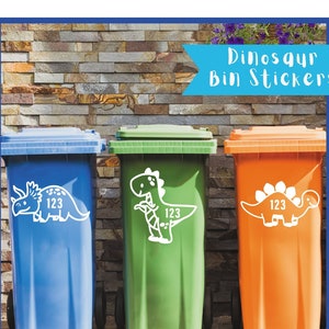 May include: Three different coloured recycling bins with dinosaur stickers. The blue bin has a triceratops, the green bin has a T-Rex, and the orange bin has a stegosaurus. Each bin has the number 123 on the sticker.