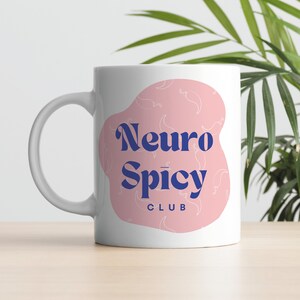 May include: White ceramic mug with a pink and white design. The mug has the text "Neuro Spicy Club" in blue.