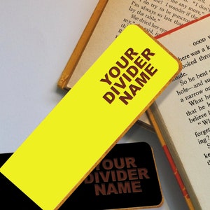 May include: A yellow bookmark with a brown border and the text "YOUR DIVIDER NAME" in brown letters. The bookmark is on top of a black bookmark with the same text.