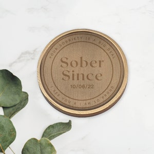 May include: A round, gold-colored metal token with the text "YOUR SOBRIETY IS A BIG DEAL" and "Sober Since 10/06/22" engraved on it. The text "I SEE YOU & I AM SO PROUD" is also engraved on the token.