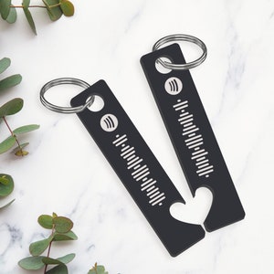 May include: Two black keyrings with silver rings. Each keyring has a heart-shaped cutout and a white Spotify logo with a barcode pattern.