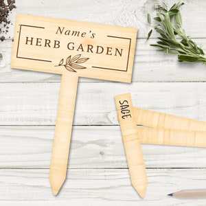 May include: Wooden herb garden sign with the text "Name's Herb Garden" and a small leaf design. A separate wooden tag with the word "Sage" is also included.