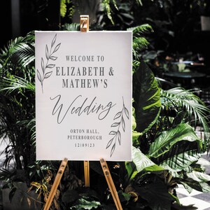 Pode incluir: Um cartaz de casamento branco com texto preto e ilustra&ccedil;&otilde;es de folhas. O cartaz diz "Bem-vindos ao casamento de Elizabeth & Mathew's Wedding, Orton Hall, Peterborough, 12109123".