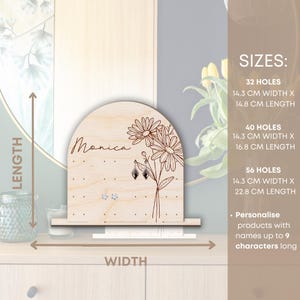 May include: Wooden earring holder with a floral design and the name "Monica" engraved on it. The holder has 32, 40, or 56 holes for earrings and measures 14.3 cm wide by 14.8 cm, 16.8 cm, or 22.8 cm long.