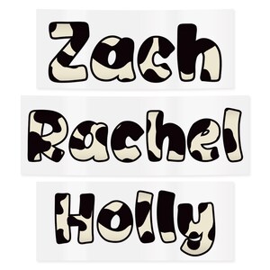 May include: Three rectangular stickers with names: "Zach", "Rachel", and "Holly". Each name is written in a bold, playful font with a black and white cow print pattern. The stickers are on a white background.