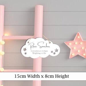 May include: White wooden cloud-shaped sign with the text "Rosie Sanchez" and the date "19.03.2024 at 13:30pm" and "Weighting 5.8 lbs". The sign is hanging from a pink ladder with a pink star light behind it. The sign measures 15 cm wide by 8 cm high.