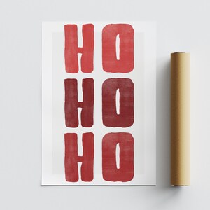 May include: A rectangular print with the words "HO HO HO" in red, block letters. The print is on white paper, and a rolled-up brown poster is next to it. The letters have a textured, painted appearance.