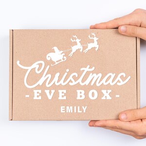 May include: A brown cardboard box with a white design of Santa Claus in a sleigh pulled by reindeer. The box says "Christmas - Eve Box - Emily".