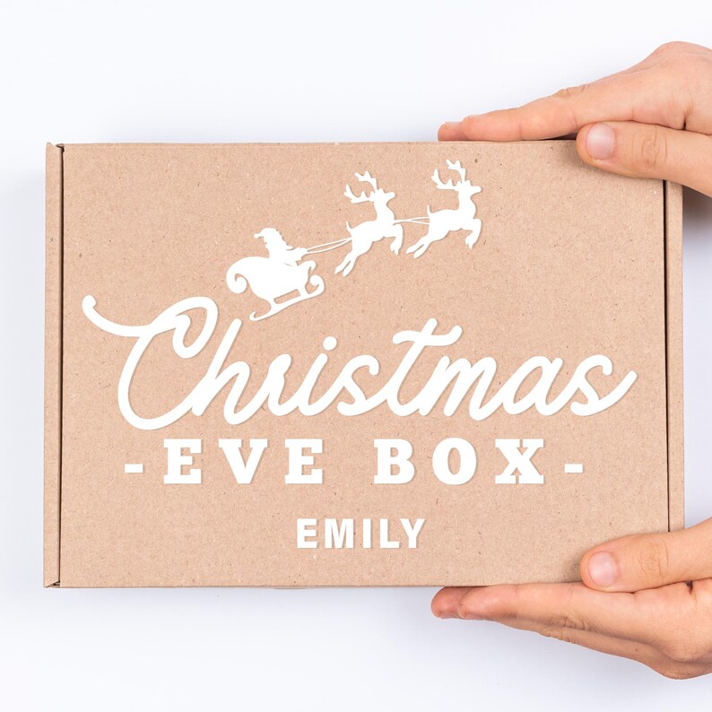 May include: A brown cardboard box with a white design of Santa Claus in a sleigh pulled by reindeer. The box says "Christmas - Eve Box - Emily".