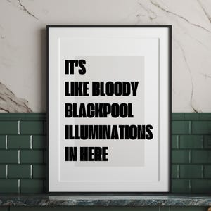 May include: A framed print with the text "IT'S LIKE BLOODY BLACKPOOL ILLUMINATIONS IN HERE" in bold black letters. The print is in a black frame and set against a light gray background. The background is a marble-like pattern.