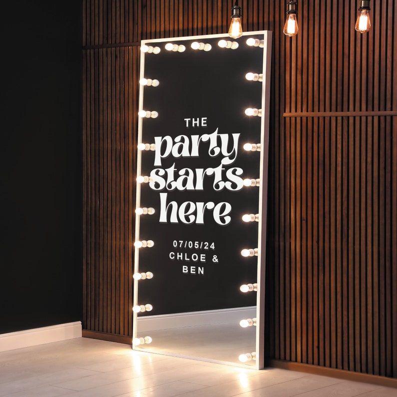 May include: A white, full-length mirror with a white frame and a black background. The mirror has a row of light bulbs around the perimeter. The mirror has the text "THE party starts here" and "07/05/24 CHLOE & BEN" written on it.