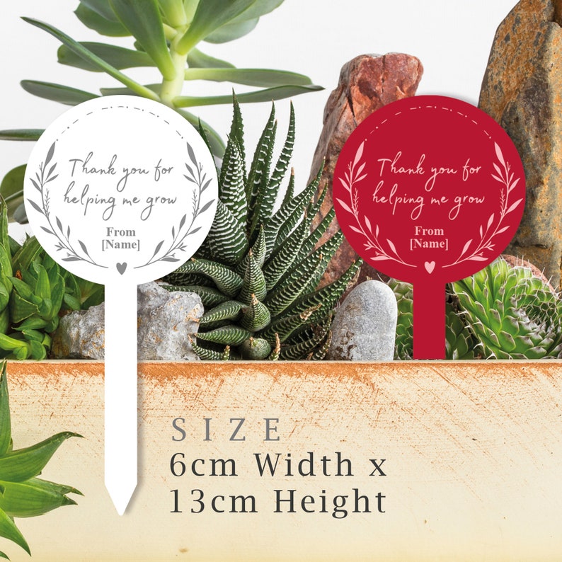 May include: Two garden stakes with a round white and red circle. The white stake has gray text that says "Thank you for helping me grow. From [Name]" and the red stake has pink text that says "Thank you for helping me grow. From [Name]" Both stakes are 6 cm wide and 13 cm high.