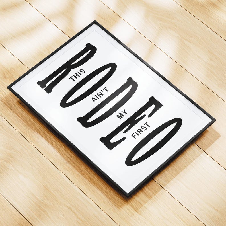 May include: Black and white framed print with the text "This ain't my first rodeo" in a bold, stylized font.