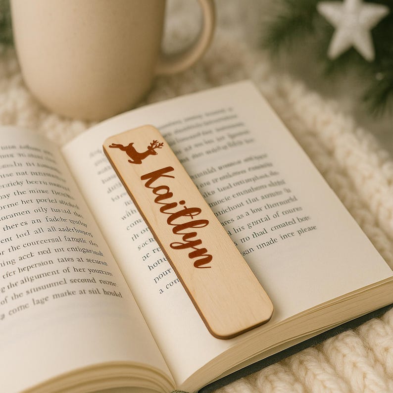 May include: A wooden bookmark with a reindeer graphic and the name "Kaitlyn" in a brown script font. The bookmark is resting on the pages of an open book. The bookmark is approximately 6 inches long.