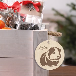 May include: A wooden gift tag with a brown silhouette of a guinea pig and the text "Piglet" on a white background.