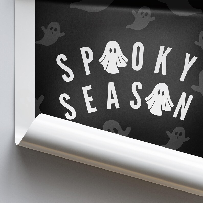 Puede incluir: Arte mural negro con tem&aacute;tica de Halloween con las palabras "Spooky Season" en blanco, letras con forma de fantasma. El fondo es negro con siluetas de fantasmas blancos tenues. El borde del arte est&aacute; curvado.