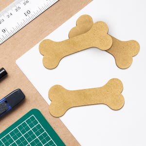 May include: Three brown wooden dog bone shaped ornaments on a white surface.