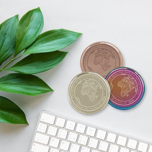 May include: Three gold-toned metal coins with the text "You make the world a better place from the class of 2024" and a world map design. The coins are on a white surface.