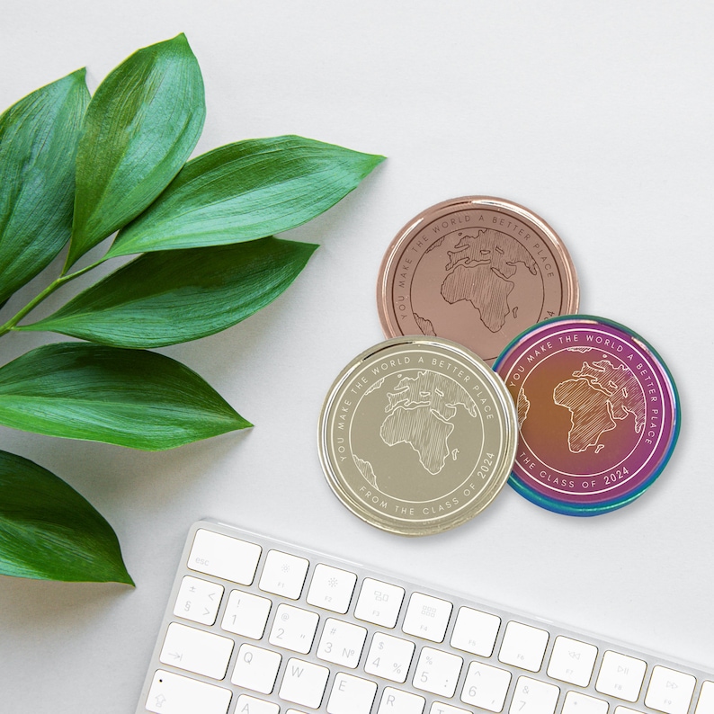 May include: Three gold-toned metal coins with the text "You make the world a better place from the class of 2024" and a world map design. The coins are on a white surface.