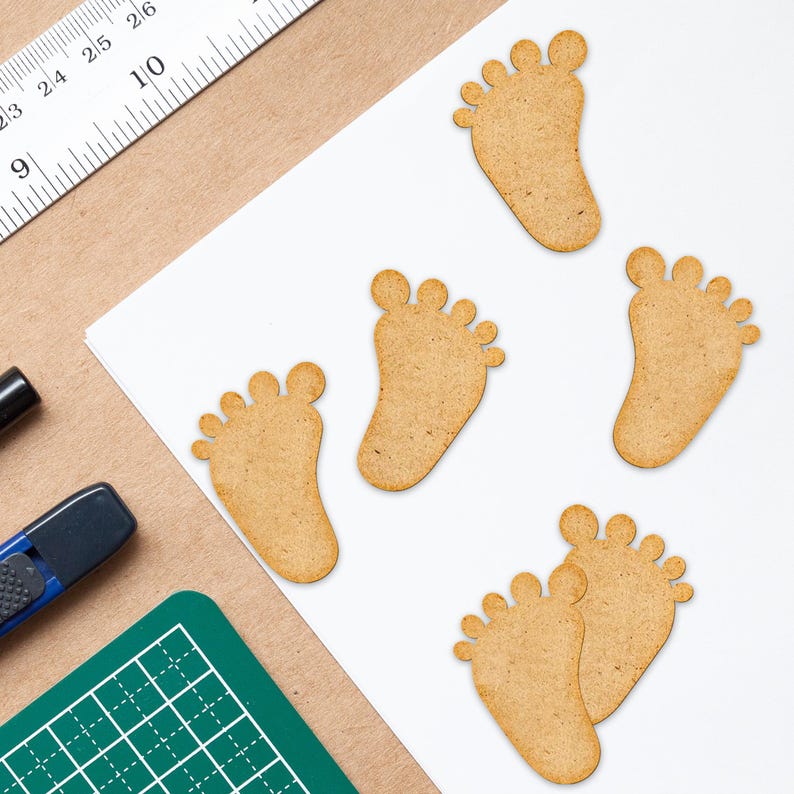 Op de afbeelding: Vijf houten uitsnijdingen van babyvoetjes. De voetjes zijn lichtbruin en hebben een natuurlijke houtnerf. De voetjes zijn willekeurig gerangschikt op een witte achtergrond.