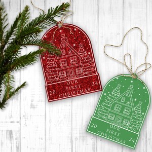 May include: Two red and green Christmas ornaments with a white outline of a house and trees. The ornaments have the text "Our First Christmas" and the numbers "20" and "24" on them.