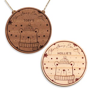 May include: Two wooden Christmas Eve box ornaments featuring a bear design. The ornaments are round and have a string for hanging. The text on the ornaments reads "Christmas Eve Box" and "TOBY'S" and "HOLLIE'S".