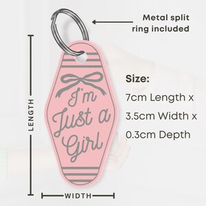 K&ouml;nnte beinhalten: Rosafarbener Schl&uuml;sselanh&auml;nger mit dem Text "I'm Just a Girl" und einem Schleifendesign. Der Schl&uuml;sselanh&auml;nger ist 7 cm lang, 3,5 cm breit und 0,3 cm tief. Inklusive Metall-Splintring.