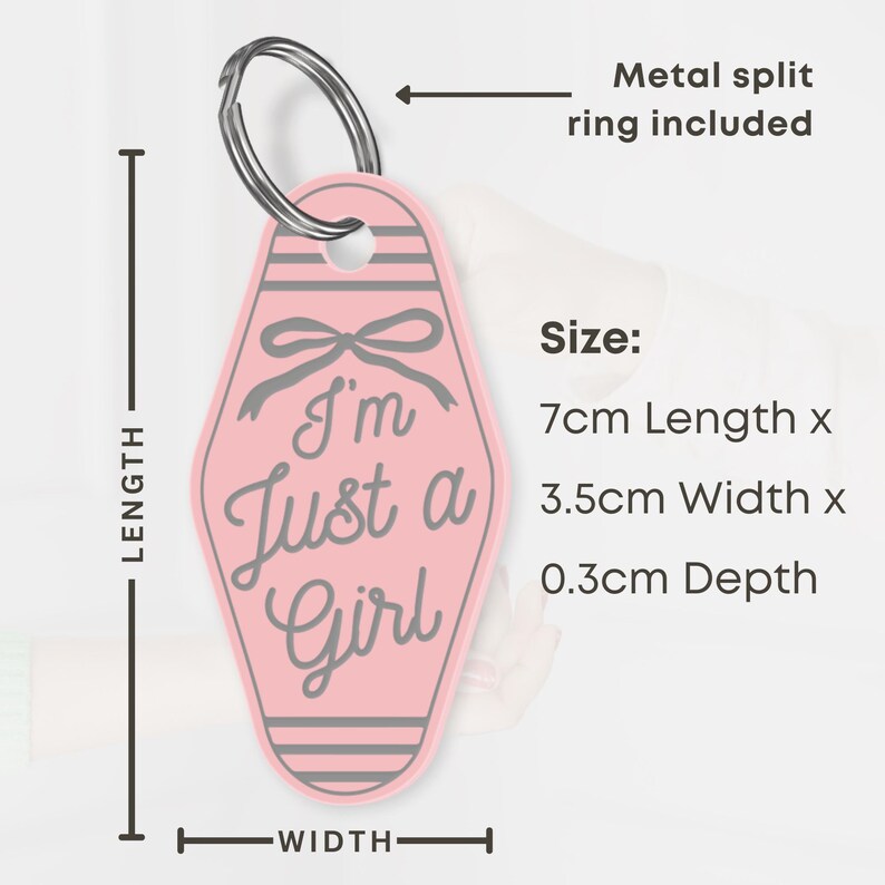 K&ouml;nnte beinhalten: Rosafarbener Schl&uuml;sselanh&auml;nger mit dem Text "I'm Just a Girl" und einem Schleifendesign. Der Schl&uuml;sselanh&auml;nger ist 7 cm lang, 3,5 cm breit und 0,3 cm tief. Inklusive Metall-Splintring.