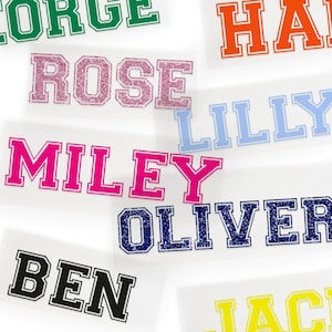 May include: A collection of iron-on name labels in various colors and fonts. The names include George, Rose, Lilly, Miley, Oliver, Ben, and Jack.
