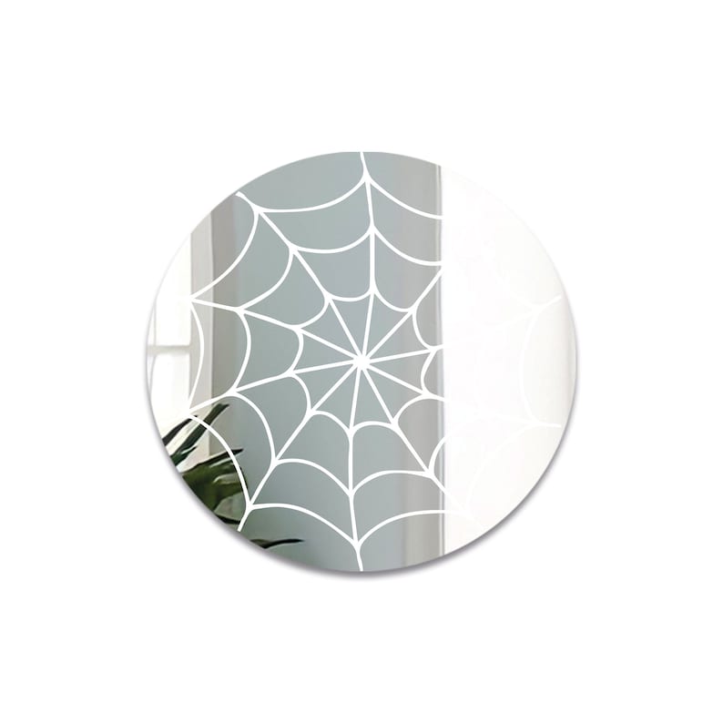 May include: A round mirror with a white spiderweb design on a gray background.
