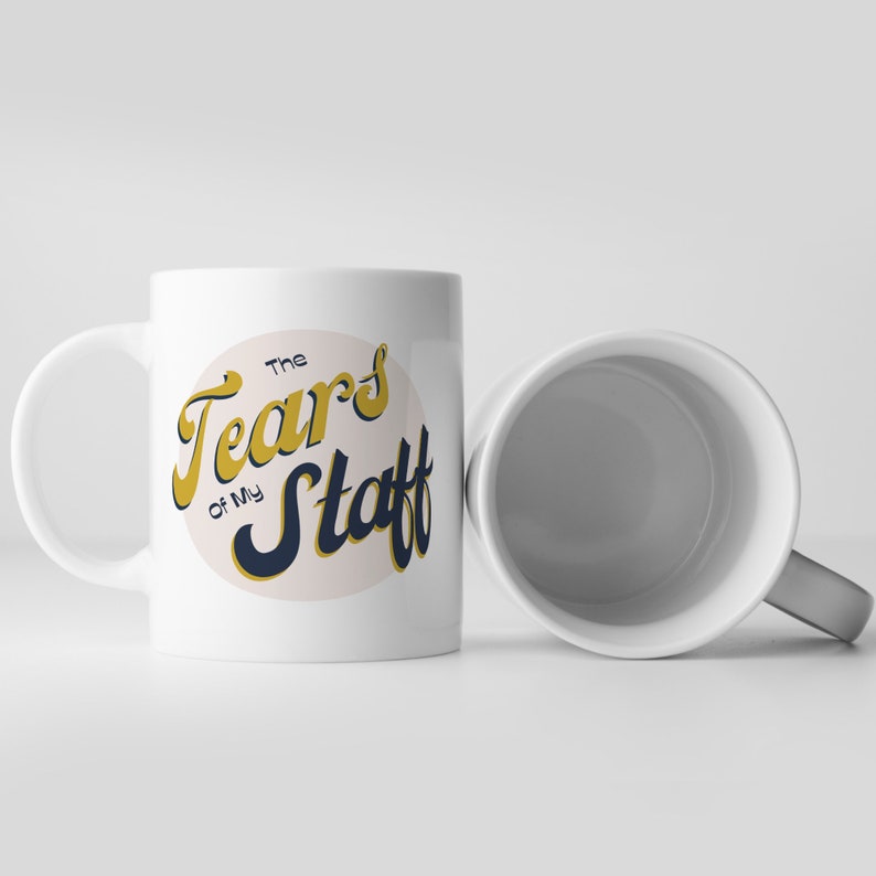 May include: White ceramic mug with a black and gold design that says "The Tears of My Staff".