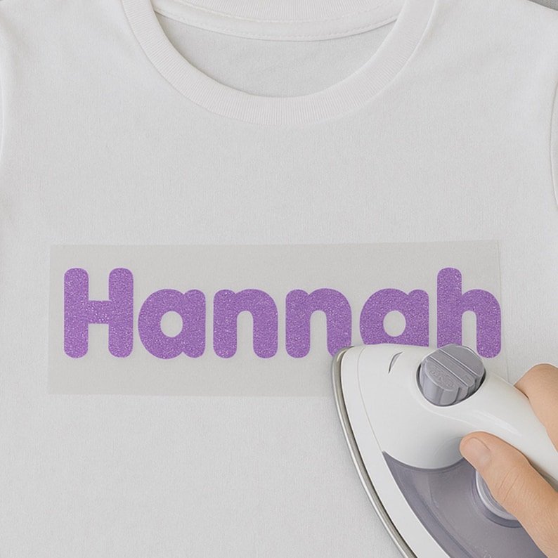 May include: A white t-shirt with a purple glitter iron-on design that says "Hannah" being ironed with a white iron.
