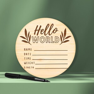 K&ouml;nnte beinhalten: Ein rundes Schild aus Holz mit dem Text "Hello World" und leeren Zeilen f&uuml;r "Name", "Datum", "Uhrzeit", "Gewicht" und "L&auml;nge".