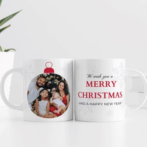May include: White ceramic mug featuring a family photo inside a Christmas ornament design. The mug has the text "We wish you a Merry Christmas and a Happy New Year" in red and gray.