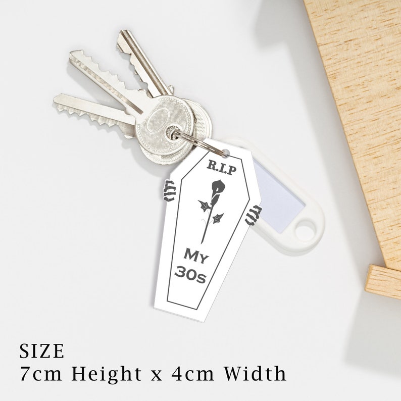 May include: White coffin-shaped keyring with a black rose and the text "R.I.P. MY 30s". The keyring is 7 cm high and 4 cm wide.