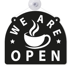 May include: Black and white cafe sign with the words "WE ARE OPEN" in a semi-circular arrangement. A white coffee cup with steam is in the center. Two white stars flank the cup. The sign is attached to a clear suction cup.