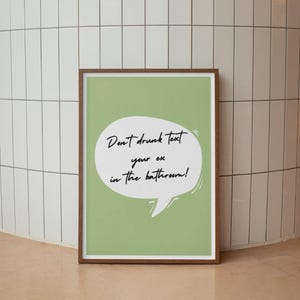 May include: A green poster with a white speech bubble that says "Don't drunk text your ex in the bathroom!" The poster is framed in a brown wood frame.