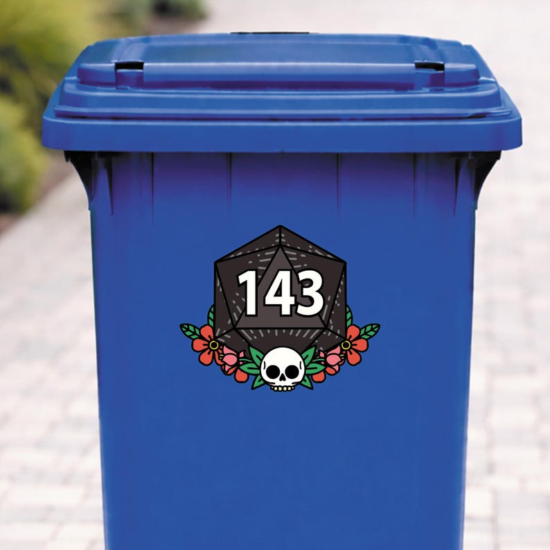 May include: A blue trash bin with a decorative sticker. The sticker features a black geometric shape with the number 143 in white, surrounded by red flowers and a skull.
