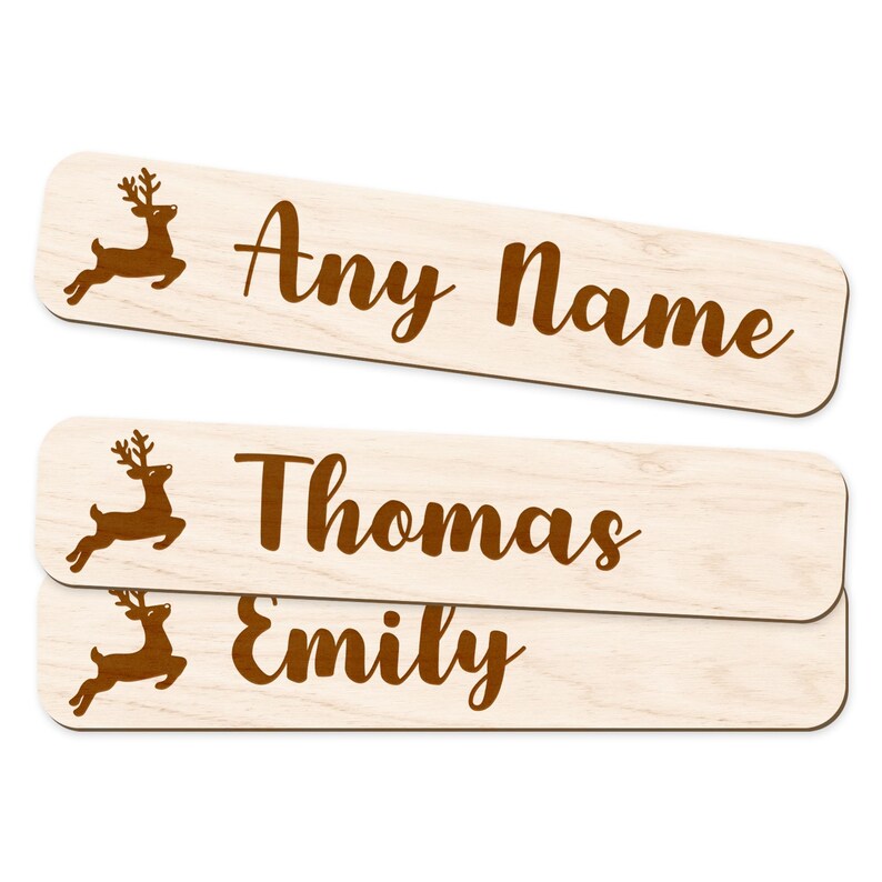 May include: Wooden name tags with a reindeer graphic. The tags are light-colored with brown text that reads "Any Name", "Thomas", and "Emily". These are ideal for Christmas gifts or holiday decor.