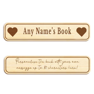 Op de afbeelding: Een houten bladwijzer met een hart aan elk uiteinde en de tekst "Any Name's Book". De onderkant van de bladwijzer heeft de tekst "Personaliseer de achterkant met je eigen bericht tot 80 tekens hier!"